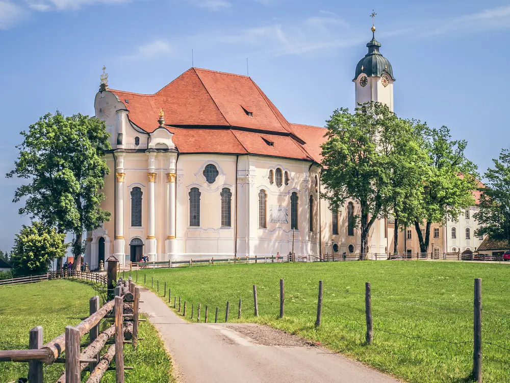 Una Wieskirche bianca in un campo a cui conduce un sentiero.