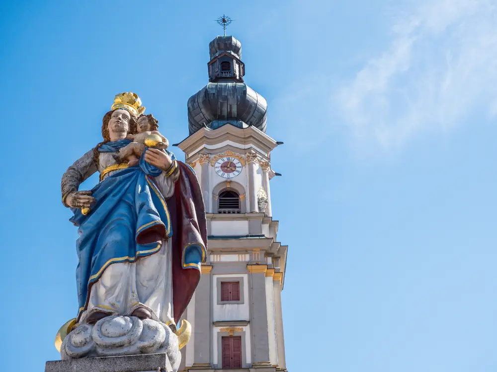 Una statua di Maria a Deggendorf davanti al campanile di una chiesa.